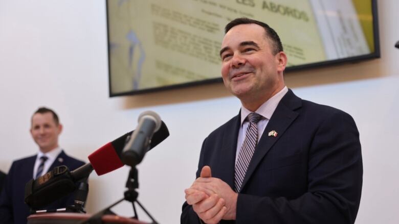 Man in suit stands at a podium with his hands clasped.