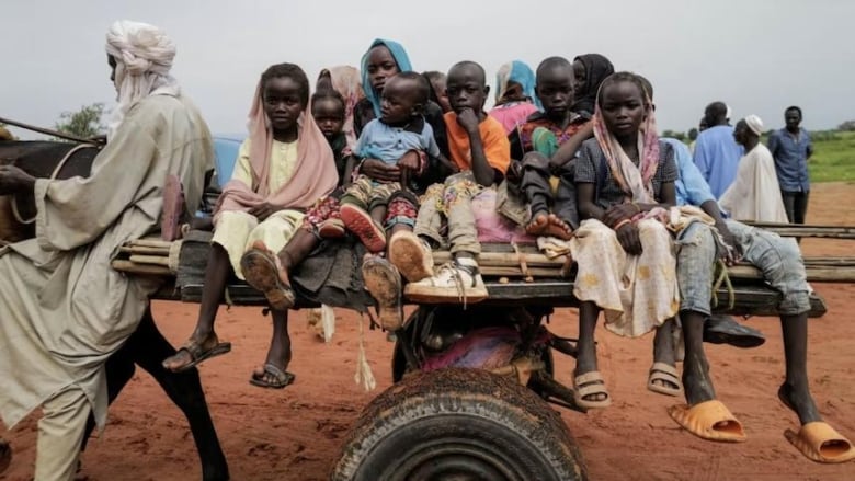 A group of children ride a cart on a dirt road. 