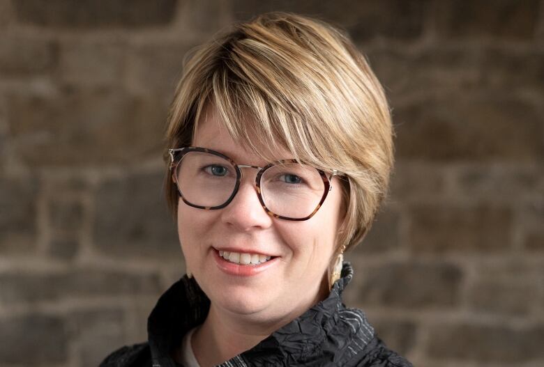 A head shot of a woman with short blond hair and glasses.