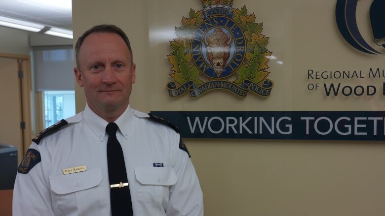 An RCMP chief stands in an office. He's in front of a Regional Municipality of Wood Buffalo RCMP sign. 