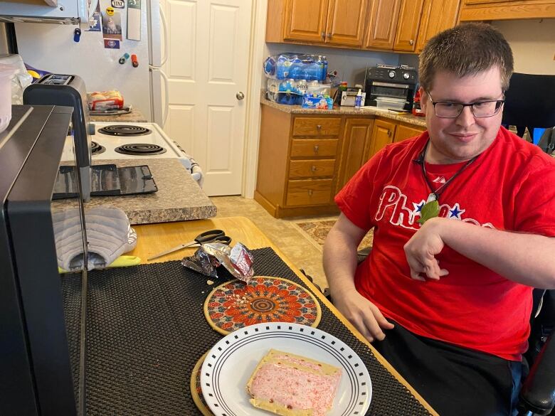 A man in a red shirt looks down at a plate of pink frosted Pop-Tarts.