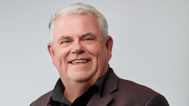 A portrait of a person in a black dress shirt and burgundy jacket. 