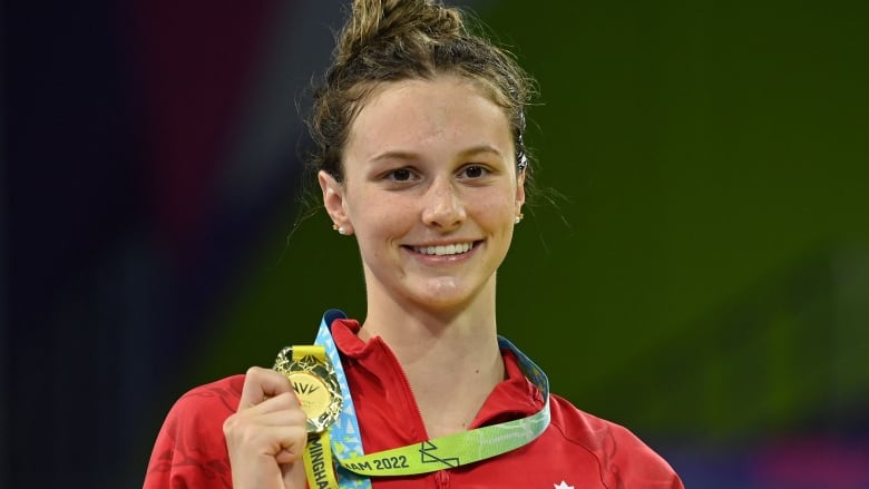 A women's swimmer hold up a gold medal.