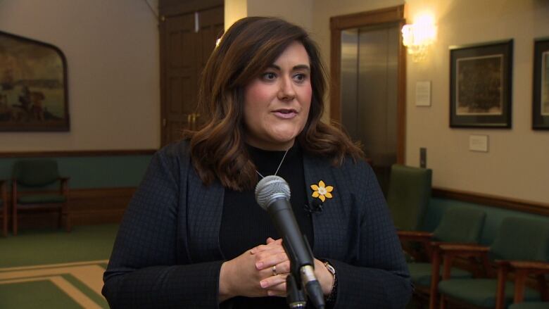 A woman with long brown hair stands in the lobby area of the House of Assembly.