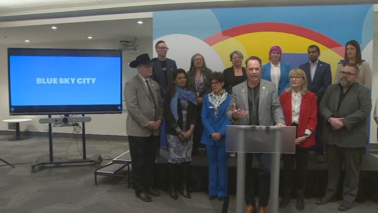 a group of people stand behind a podium. a screen that reads blue sky city is in the background.