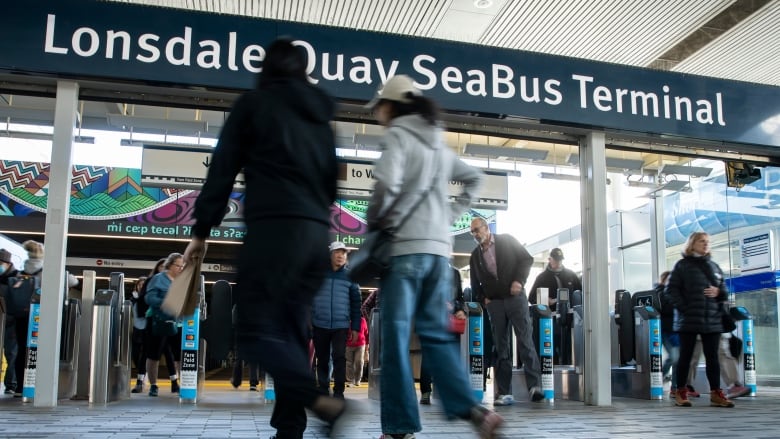 People walk in and out of gates under a sign that says Lonsdale Quay SeaBus Terminal.