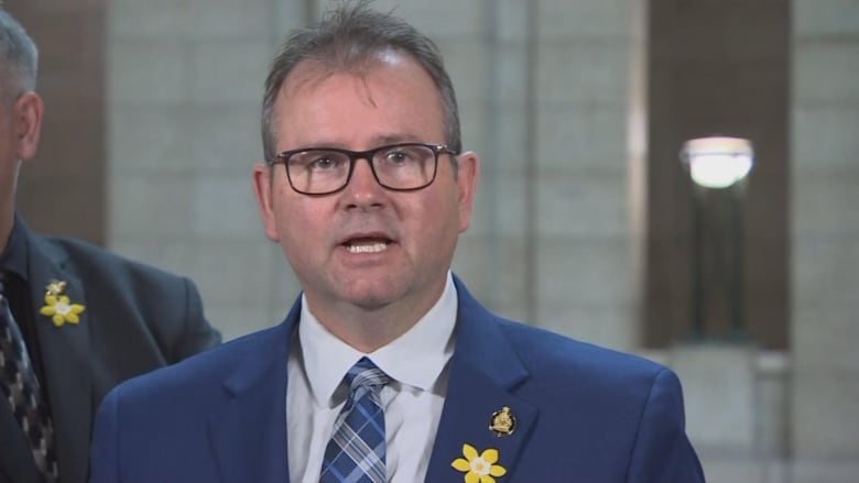 A man wearing glasses and a suit and tie is pictured.