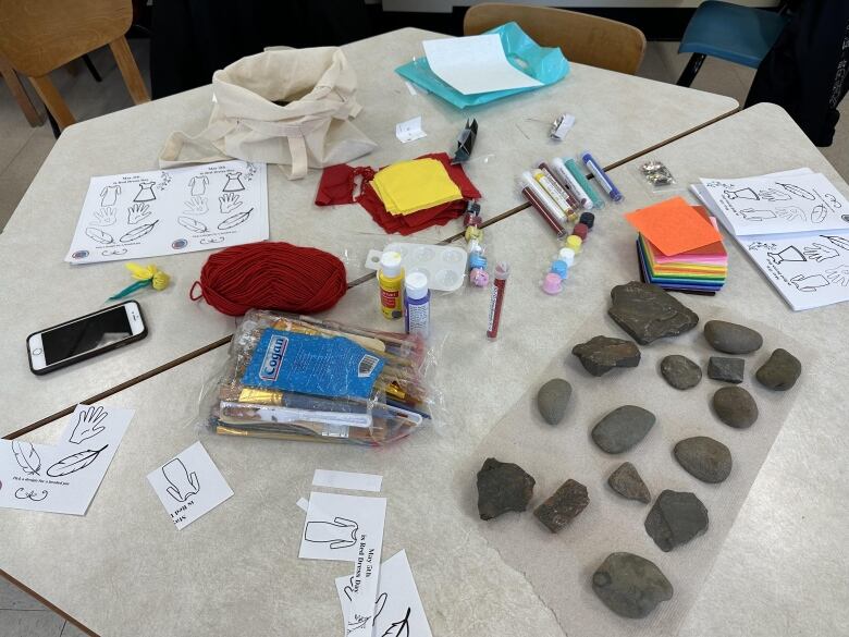 A table in the shape of a hexagon is cluttered with crafting supplies and several, palm-sized stones.