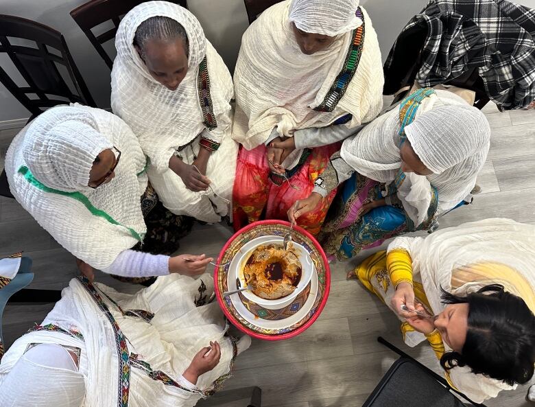 Women sit in a circle around a large bowl of porridge.