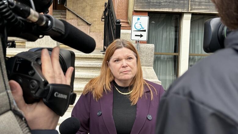 Medium shot of woman in purple suit framed by two journalists