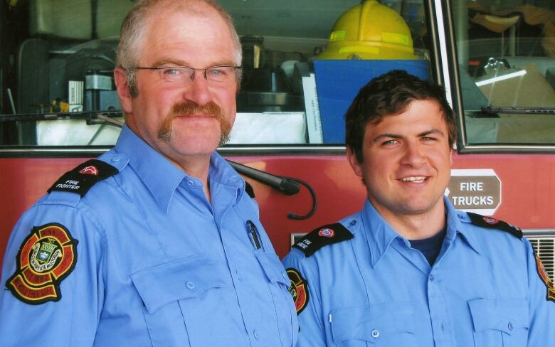 A father and son wearing firefighting uniforms are pictured in front of a fire truck.