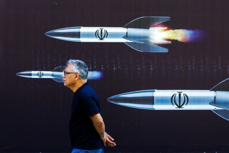 A man walks past a banner depicting missiles on a street in Tehran.