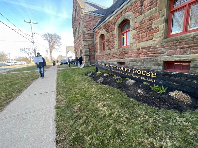 A stone courthouse with someone walking along the sidewalk holding a sign. 