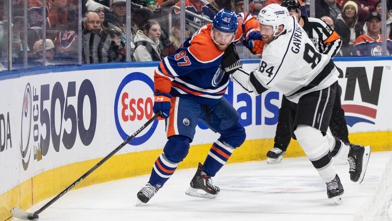 One hockey player in blue tries to hold off a hockey player in white. 