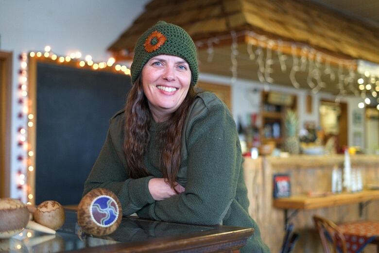 A woman with long brown hair in a green sweater and green tuque smiles during an interview. 