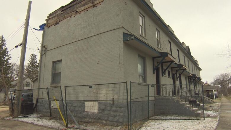 A row of brick townhouses is shown in this picture. The wall facing the camera is missing bricks at the top. 