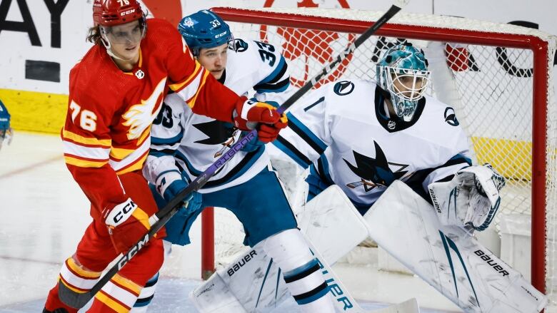 Two hockey players fight for position in front of a goalie.