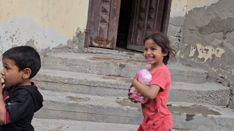 A small child, dressed in pink, holds a pink bag containing the food to her chest. She has a big smile.  