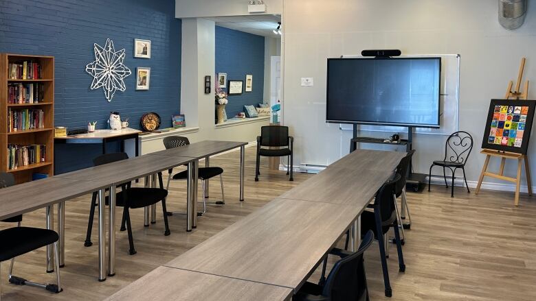 An empty classroom with a book shelf, desks, and a smart board. 