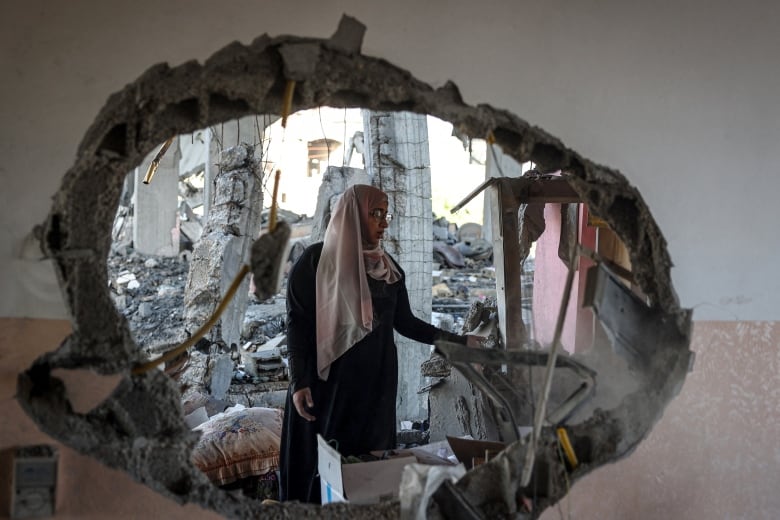 A hole in the wall frames a person standing amid the rubble.