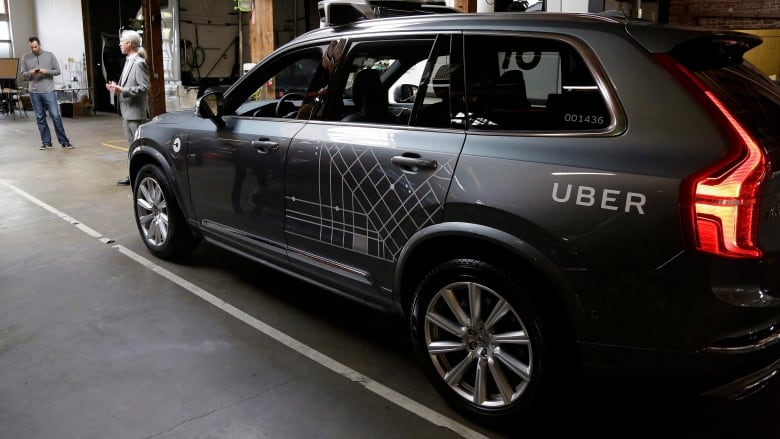 A car with sensors above it marked 'Uber' lies parked, with two people in front of it.