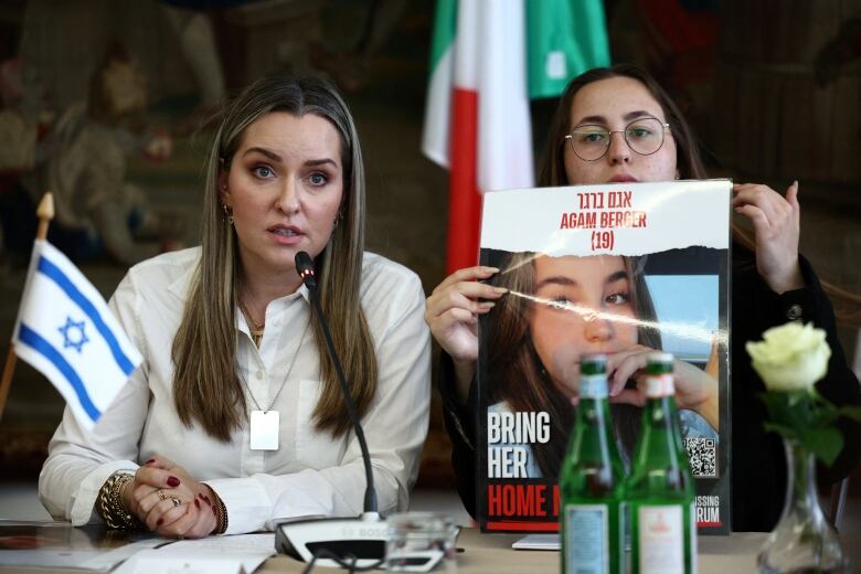 Two women sit at a table and the one on the right holds a photo.