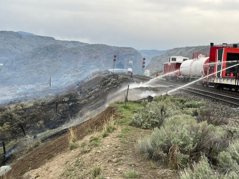 A train with water hose attachments puts out a patch of singed grass next to the tracks.