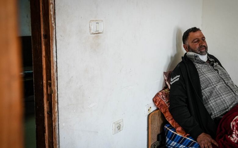 A wounded person sits on a bed against a wall.