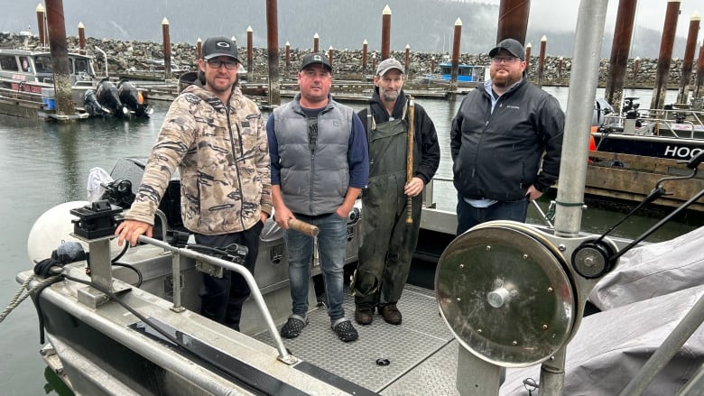 four men stand on a boat in a marina