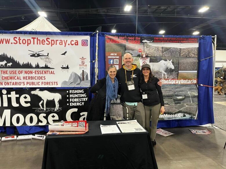 Three people standing in front of a booth at a tradeshow. 