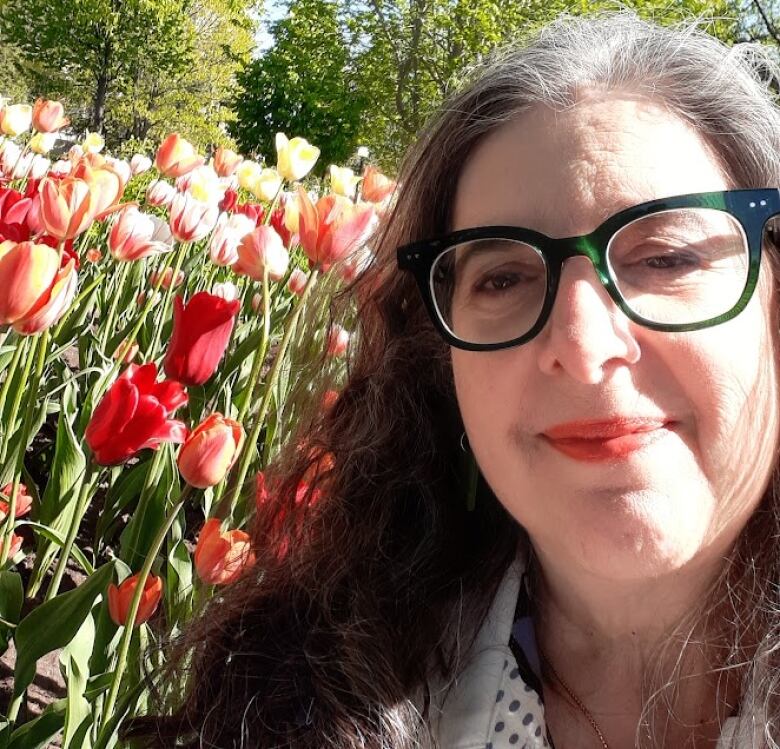 A rabbi wearing glasses and posing with red and pink tulips. 