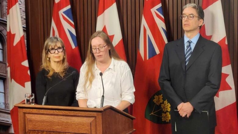 A person speaks at a lectern, flanked by two others.