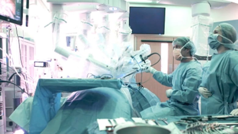 Two medical professionals in full protective gear use robotic equipment to operate.