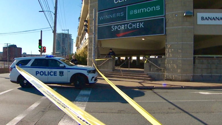 A police vehicle and tape block a pedestrian entrance to a parking garage. 