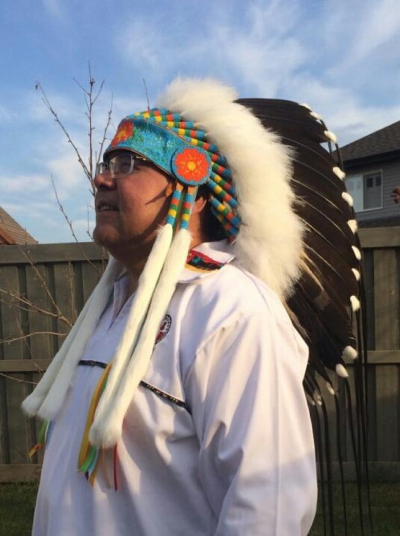 A man stands wearing a feathered headdress.