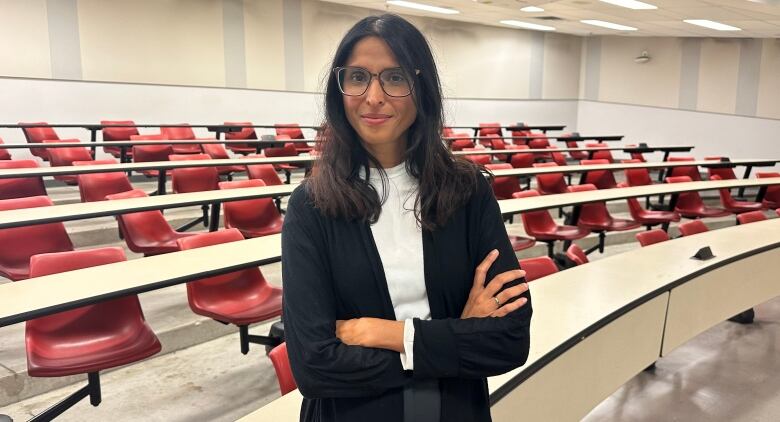 Photo of Rupa Banerjee standing in front of empty desks in a classroom. 