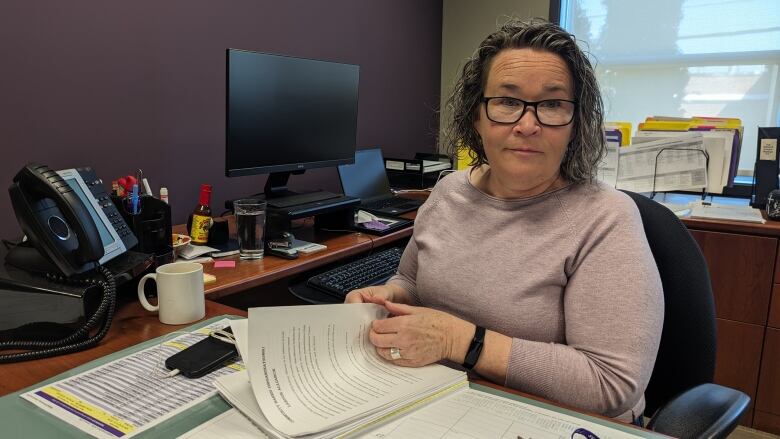 A woman in glasses at a desk flipping through papers