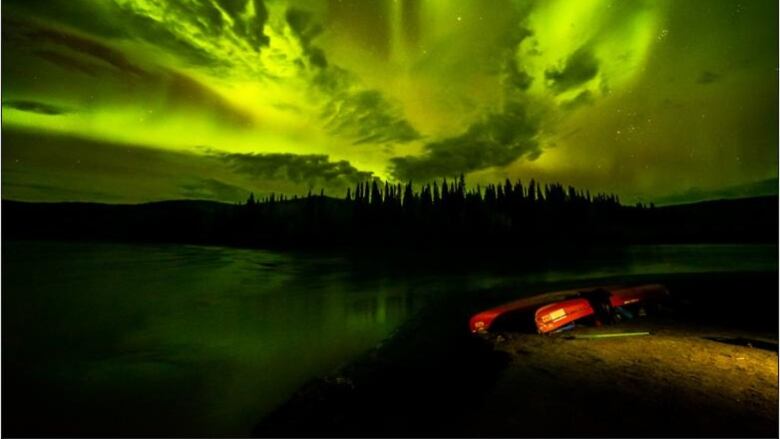 Canoes are seen on shore under bright northern lights.