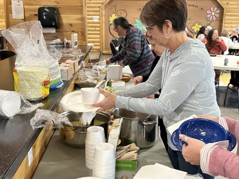 A woman with short brown hair spoons soup into a Styrofoam bowl. 