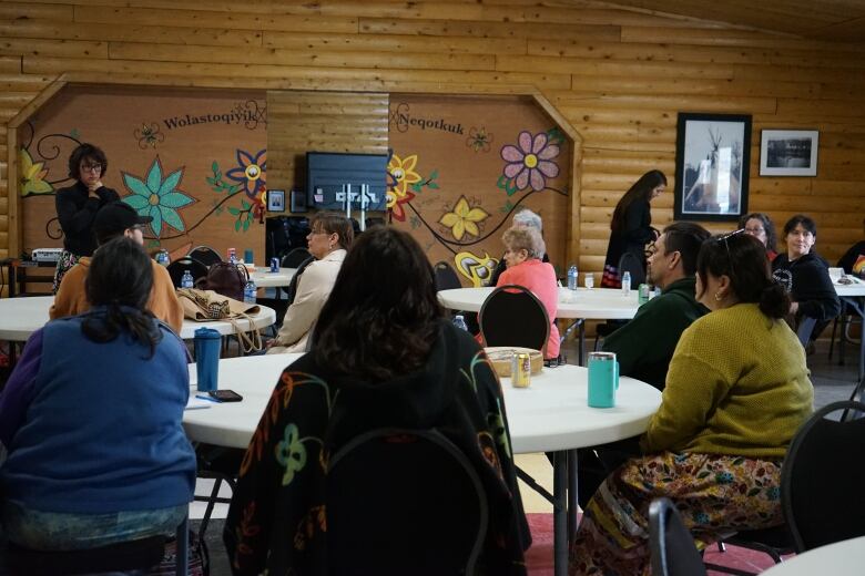 People sit around circular white tables in a room with wooden walls.