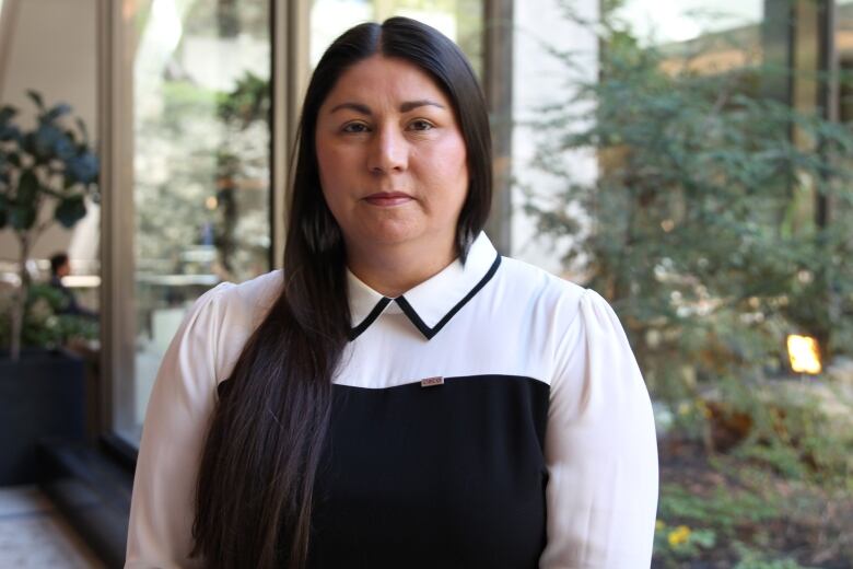 A woman with long black hair and a white and black dress with long sleeves stands near a courtyard garden in a hotel lobby.  