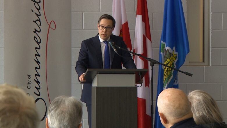 A man with short dark hair, glasses and a suit speaks at a podium in front of a City of Summerside sign.