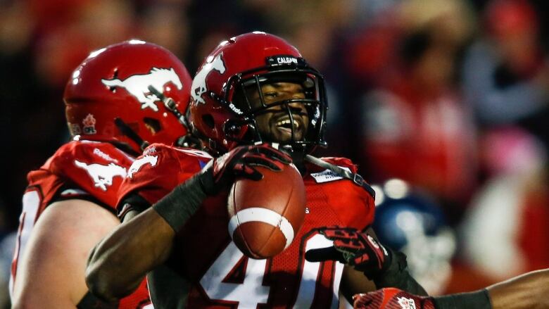 a football player holding a ball celebrates post play with two teammates all in red and white jerseys.