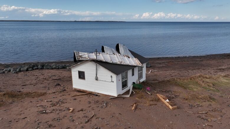 A home with half of its roof torn off on a beach right by the shoreline.