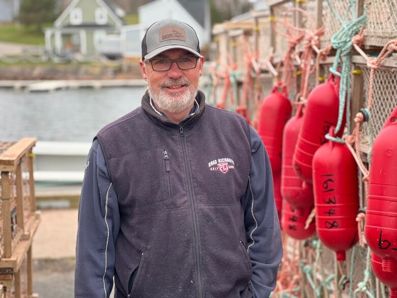 A man stands next to some lobster traps with red buoys 