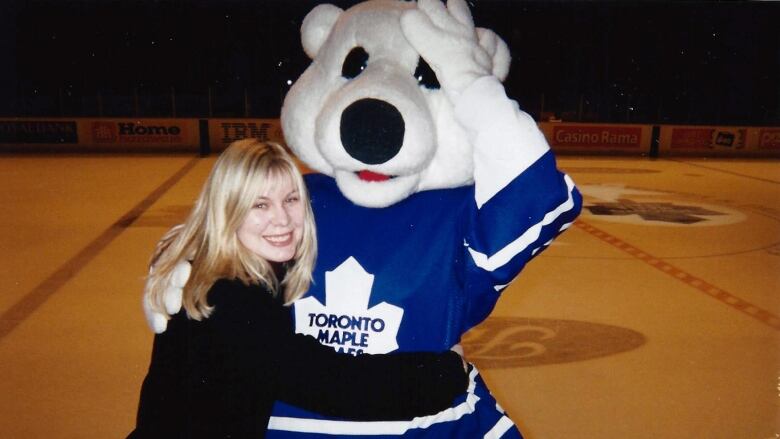 A woman hugs a mascot in front of a rink.