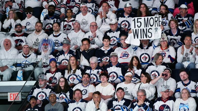 Fans wearing white sit in the stands, with one holding a sign that reads, '15 more wins.'