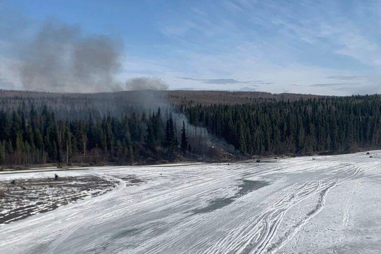 Smoke is seen billowing from a spot at the edge of a forested area.