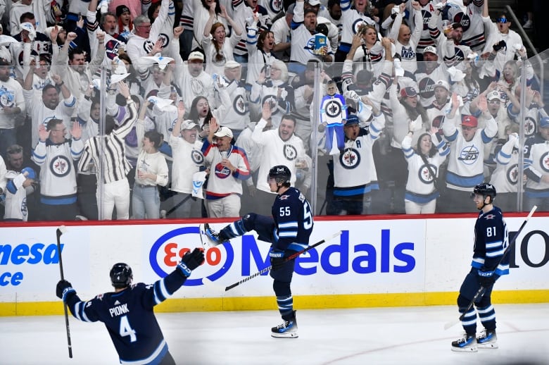 Jets players celebrate in the foreground while Jets fans wearing white cheer behind the glass.