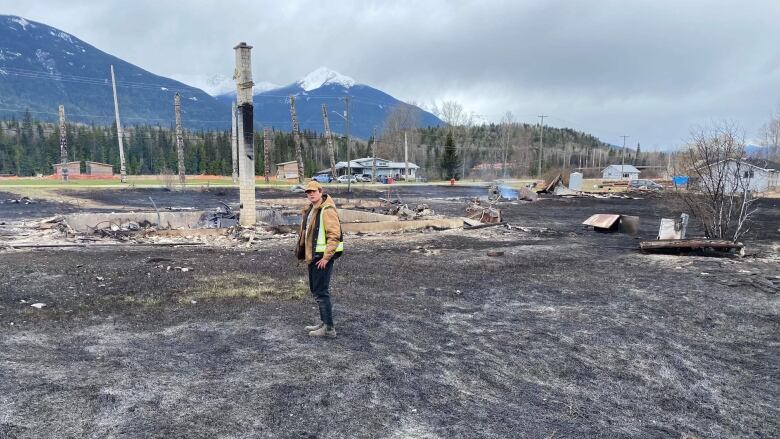 A person stands on burned ground with a chimney nearby.